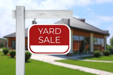 Sign with text YARD SALE and blurred view of modern house on sunny day