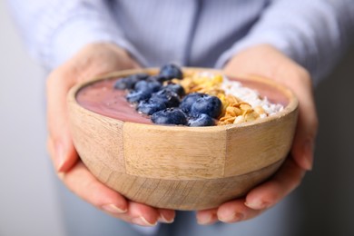 Photo of Woman holding bowl of delicious fruit smoothie with fresh blueberries, granola and coconut flakes, closeup