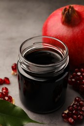 Glass jar of tasty pomegranate sauce and fresh ripe fruit on light grey table