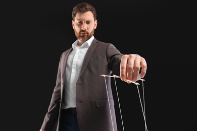 Photo of Man in suit pulling stringspuppet on black background, low angle view