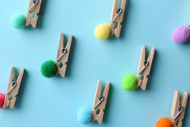 Photo of Clothespins with small soft balls on light blue background, flat lay