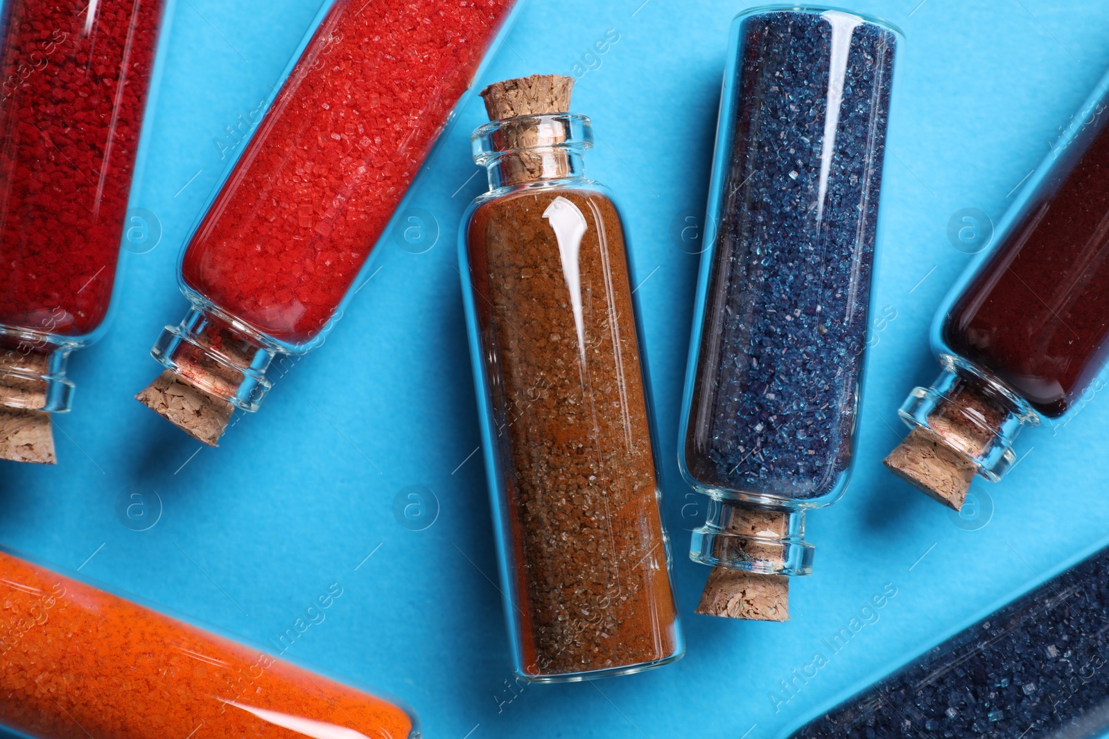 Photo of Glass bottles with different food coloring on light blue background, flat lay