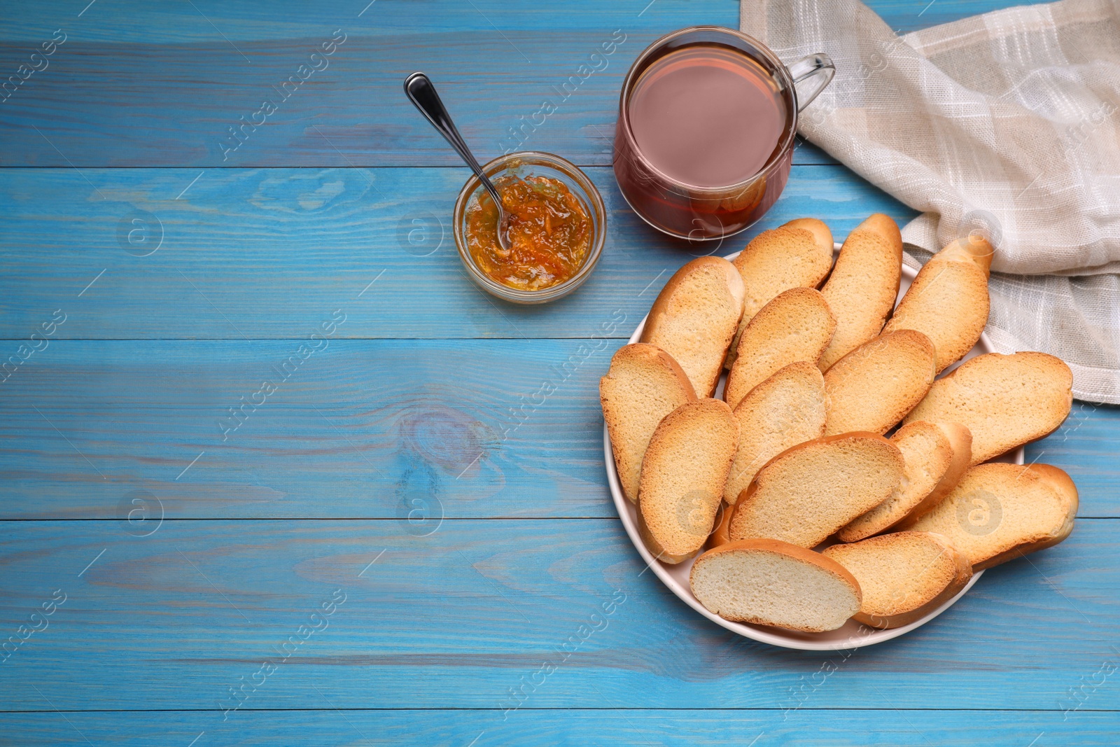 Photo of Hard chuck crackers, jam and cup of tea on light blue wooden table, flat lay. Space for text