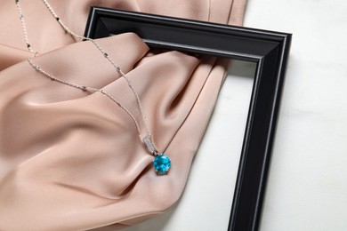 Beautiful necklace with light blue gemstone, beige fabric and black frame on white background, flat lay. Luxury jewelry