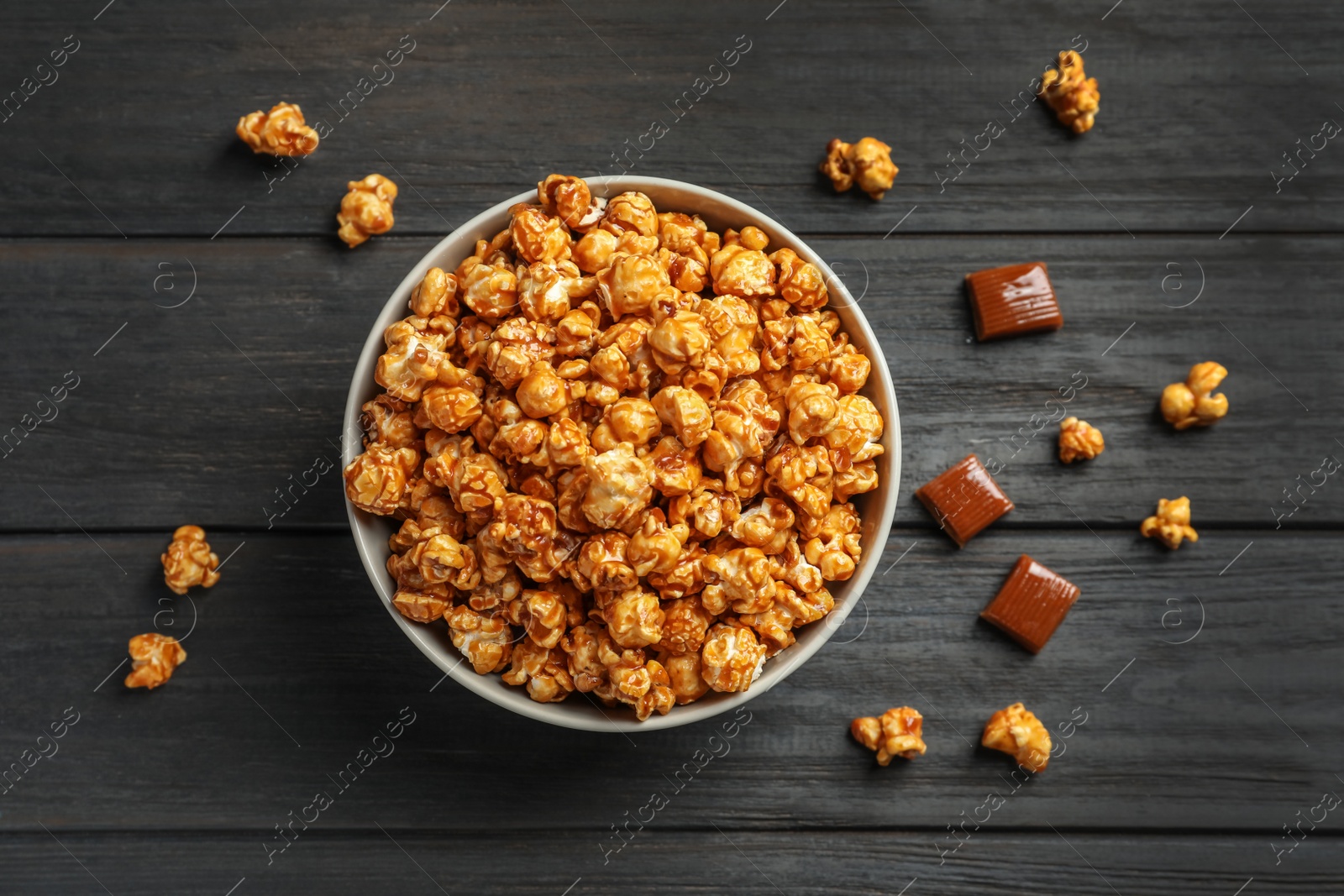 Photo of Delicious popcorn with caramel in bowl and candies on wooden background, top view