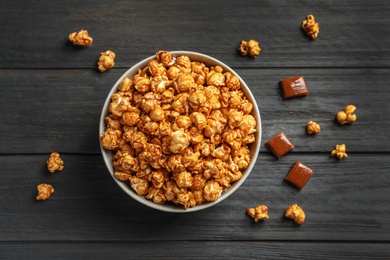 Photo of Delicious popcorn with caramel in bowl and candies on wooden background, top view