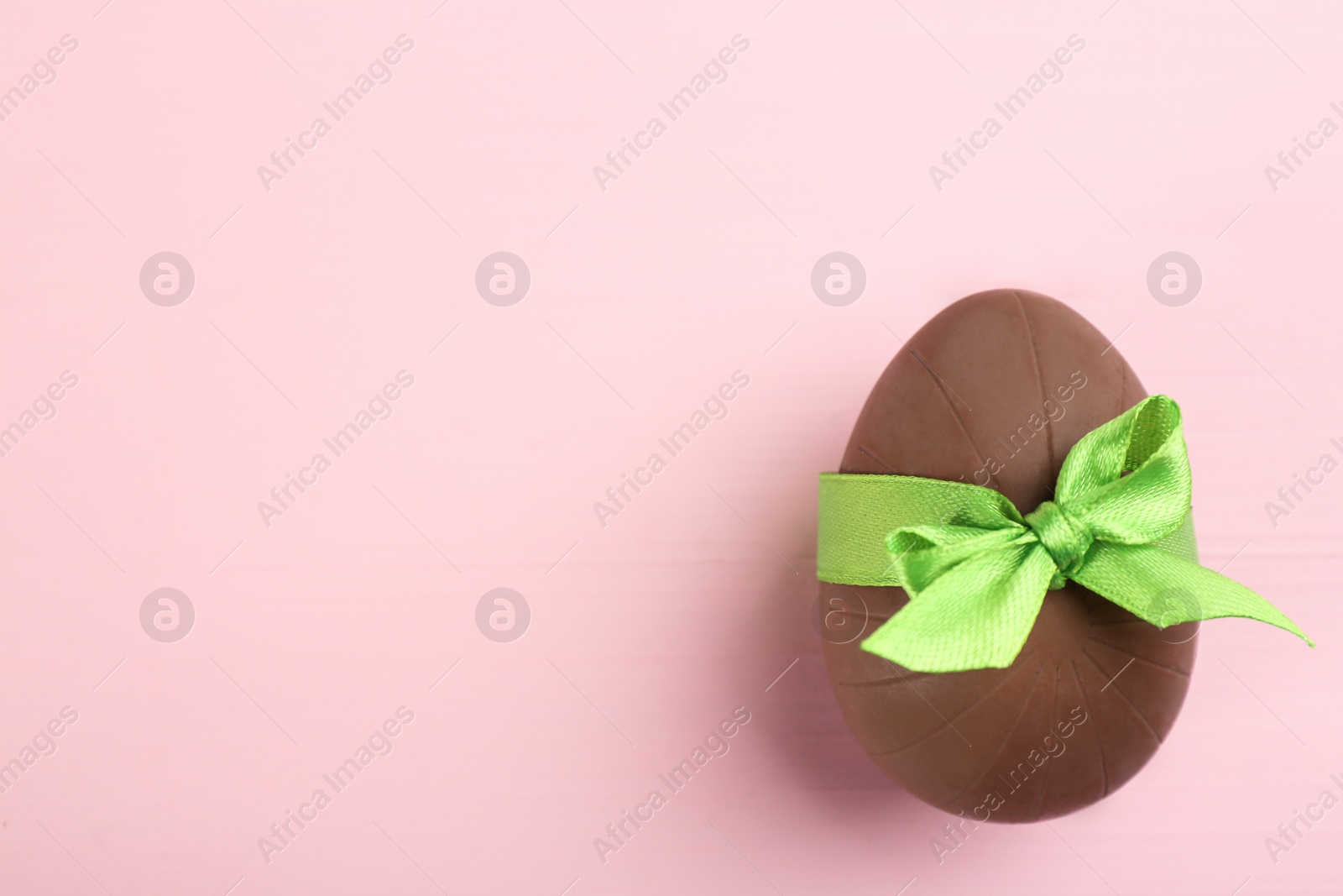 Photo of Sweet chocolate egg with green bow on pink wooden table, top view. Space for text