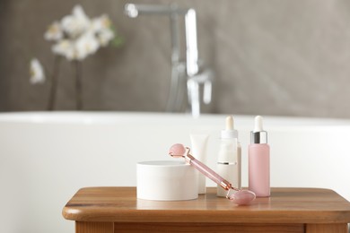 Photo of Natural face roller and cosmetic products on wooden table in bathroom. Space for text