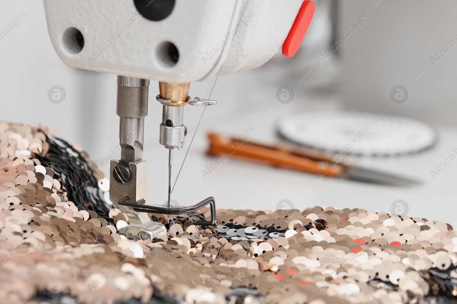 Photo of Sewing machine and beautiful fabric with paillettes indoors, closeup