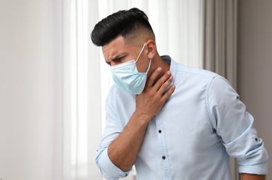 Photo of Man in medical mask suffering from pain during breathing indoors