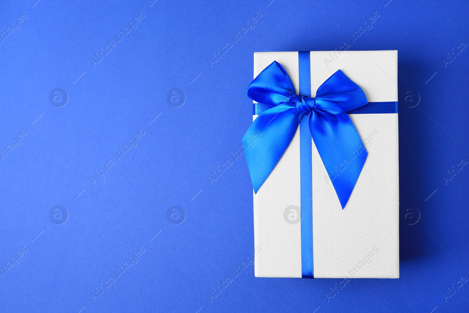 Photo of Beautiful gift box with bow on blue background, top view. Space for text