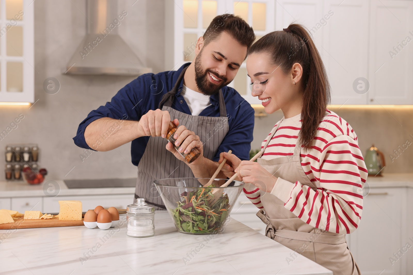 Photo of Happy affectionate couple cooking together at white table in kitchen