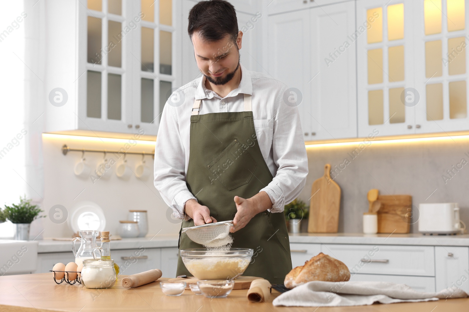 Photo of Making bread. Man sprinkling flour onto dough at wooden table in kitchen