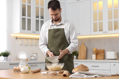 Making bread. Man sprinkling flour onto dough at wooden table in kitchen