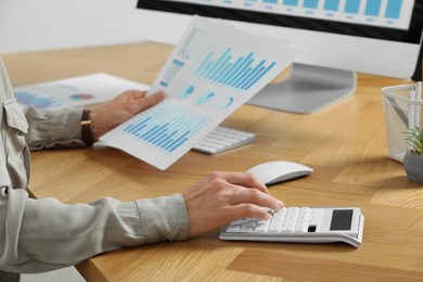 Professional accountant using calculator at wooden desk in office, closeup