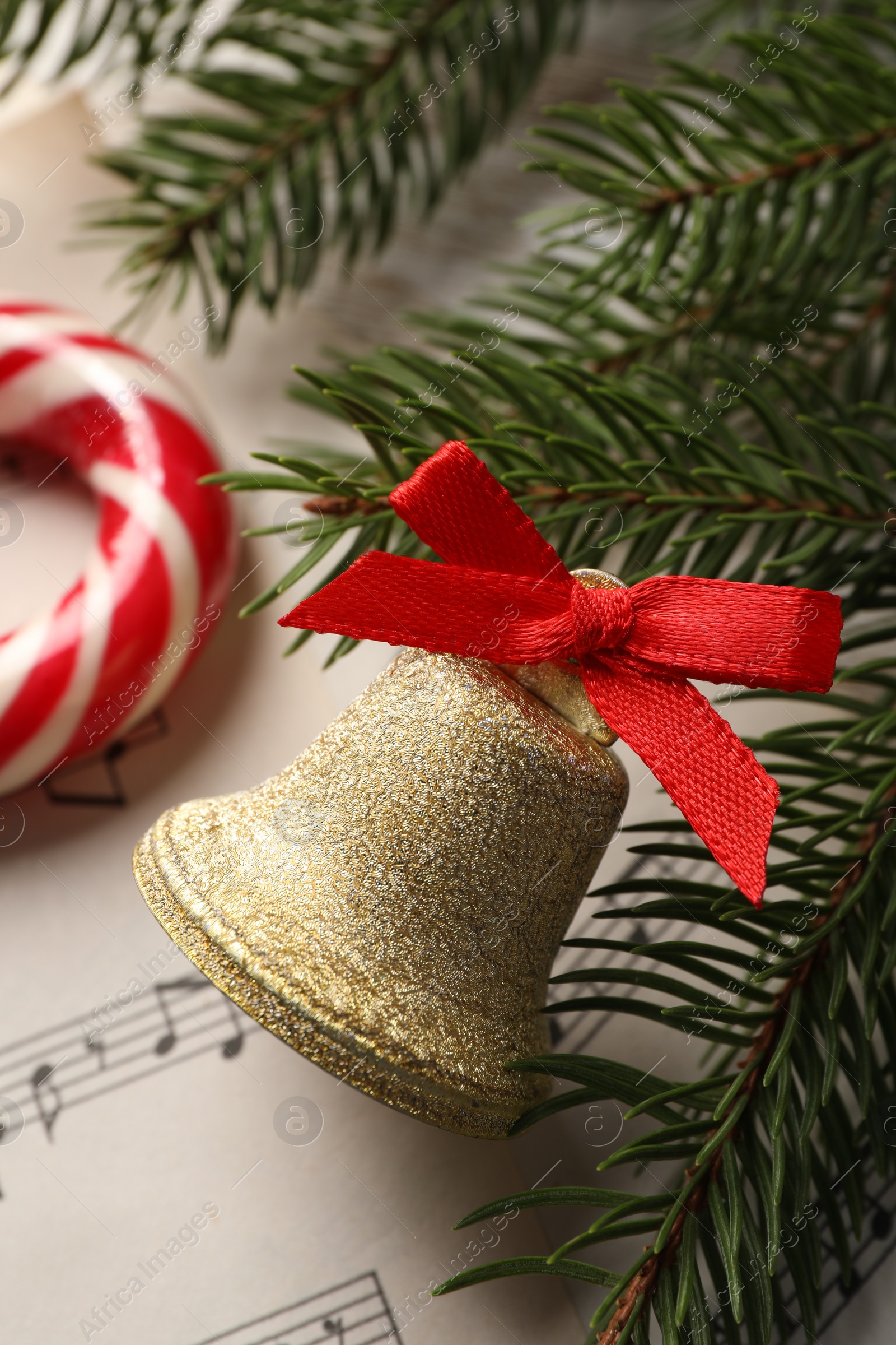 Photo of Golden shiny bell with red bow and fir branches on music sheet, closeup. Christmas decoration