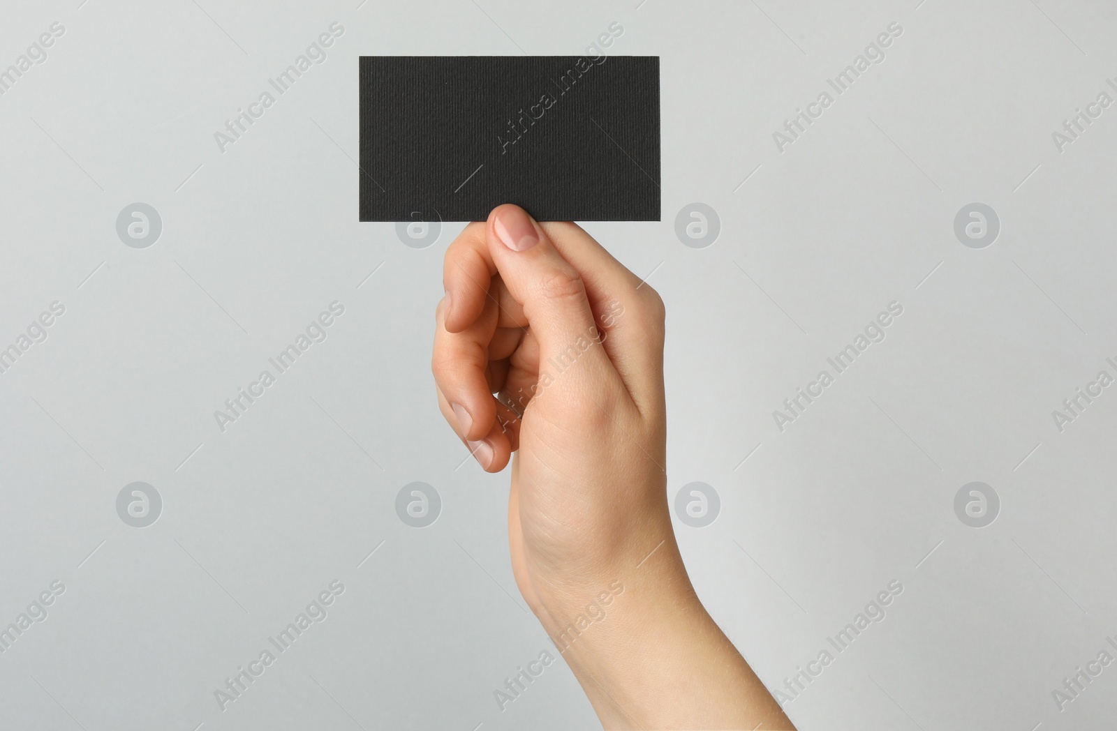 Photo of Woman with blank black business card on light grey background, closeup. Mockup for design