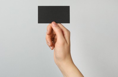 Photo of Woman with blank black business card on light grey background, closeup. Mockup for design