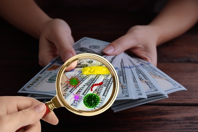 Image of Woman with magnifying glass detecting microbes on dollar banknotes, closeup