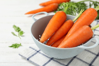 Photo of Carrots in colander on white table, closeup