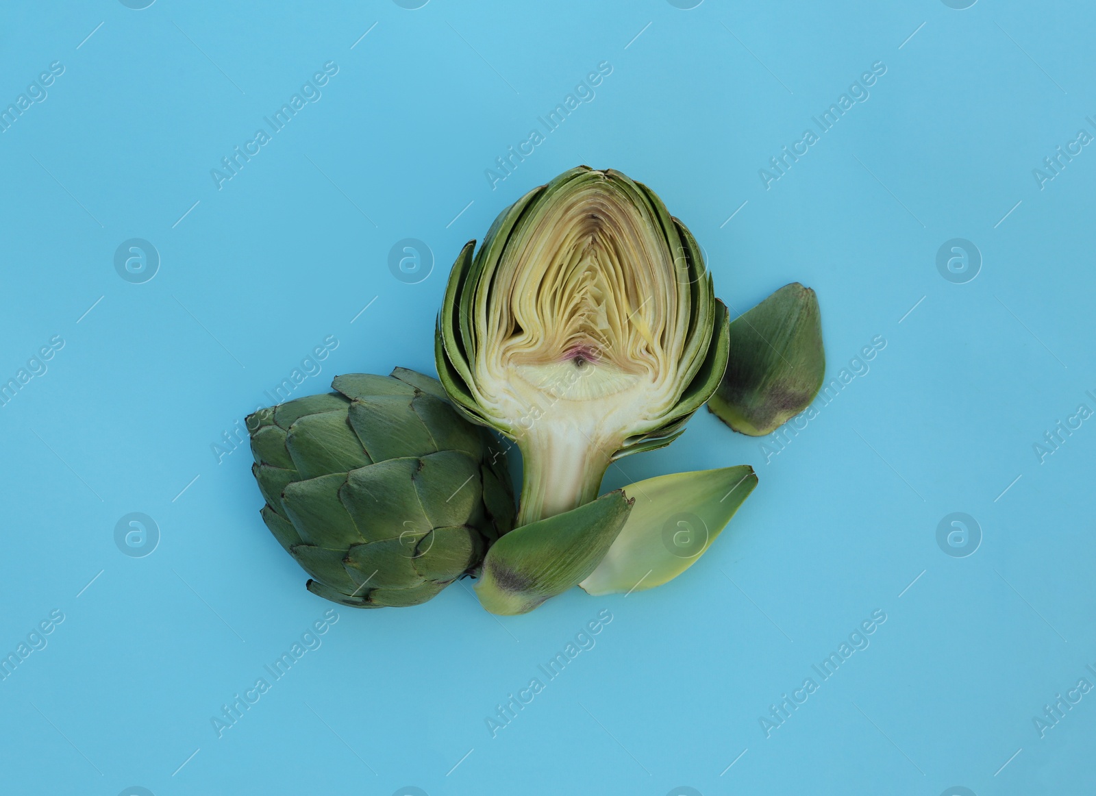 Photo of Cut fresh raw artichoke on light blue background, flat lay