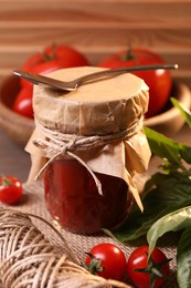 Photo of Jar of tasty tomato paste with spoon, ingredients and thread on table