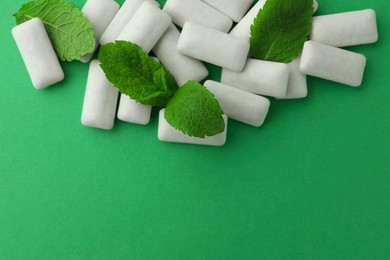 Tasty white chewing gums and mint leaves on green background, top view. Space for text