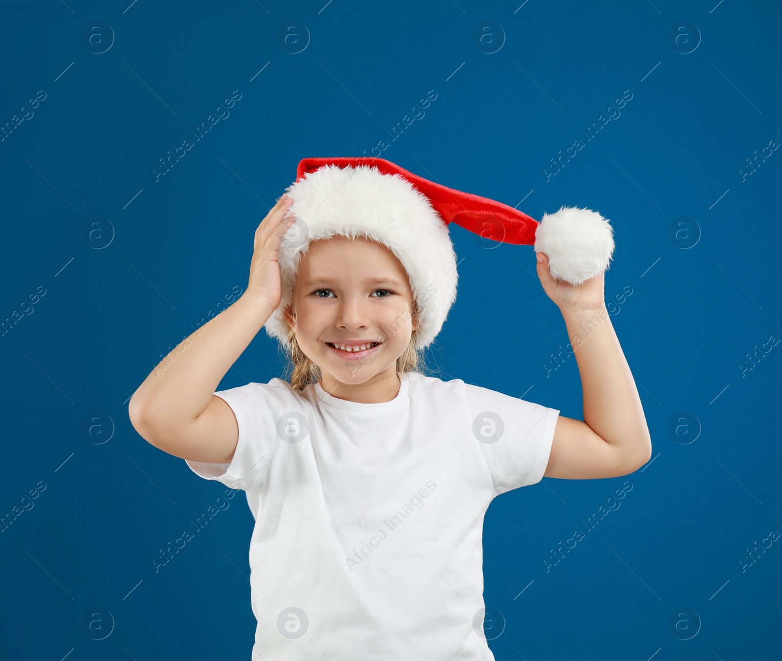 Photo of Cute little child wearing Santa hat on blue background. Christmas holiday