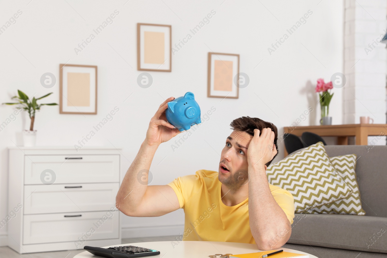 Photo of Sad man looking for money in piggy bank at table indoors