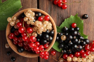 Different fresh ripe currants and green leaves on wooden table, flat lay