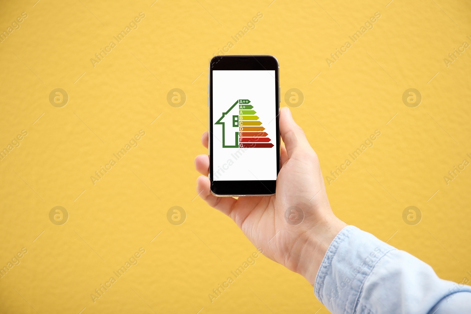 Image of Energy efficiency rating on smartphone display. Man holding device on orange background, closeup