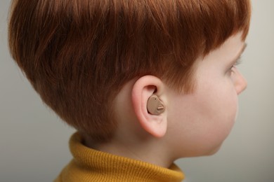 Photo of Little boy with hearing aid on grey background, closeup