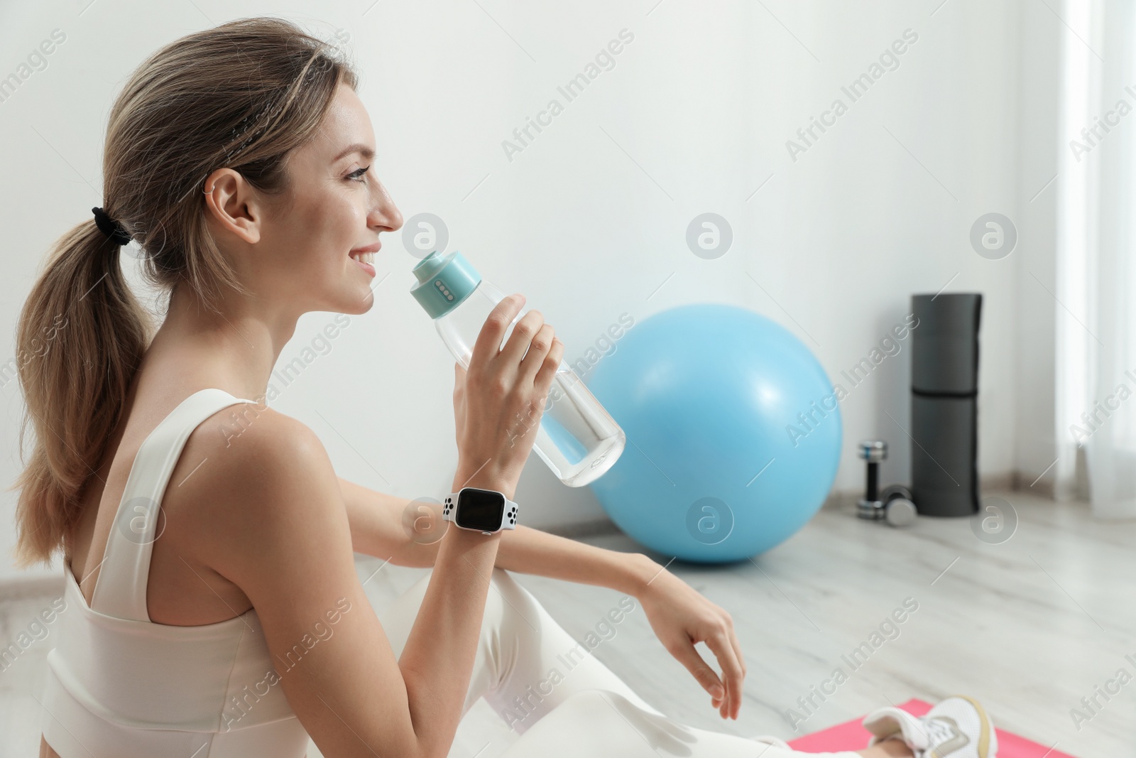 Photo of Young woman with smart watch drinking water indoors, space for text