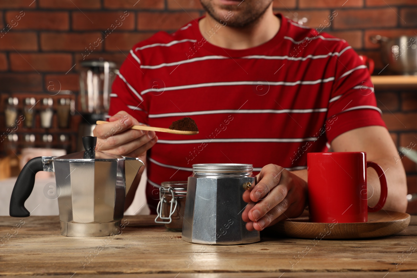Photo of Man putting ground coffee into moka pot at wooden table in kitchen, closeup