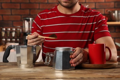 Photo of Man putting ground coffee into moka pot at wooden table in kitchen, closeup