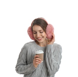 Happy woman with cup of drink wearing warm earmuffs on white background