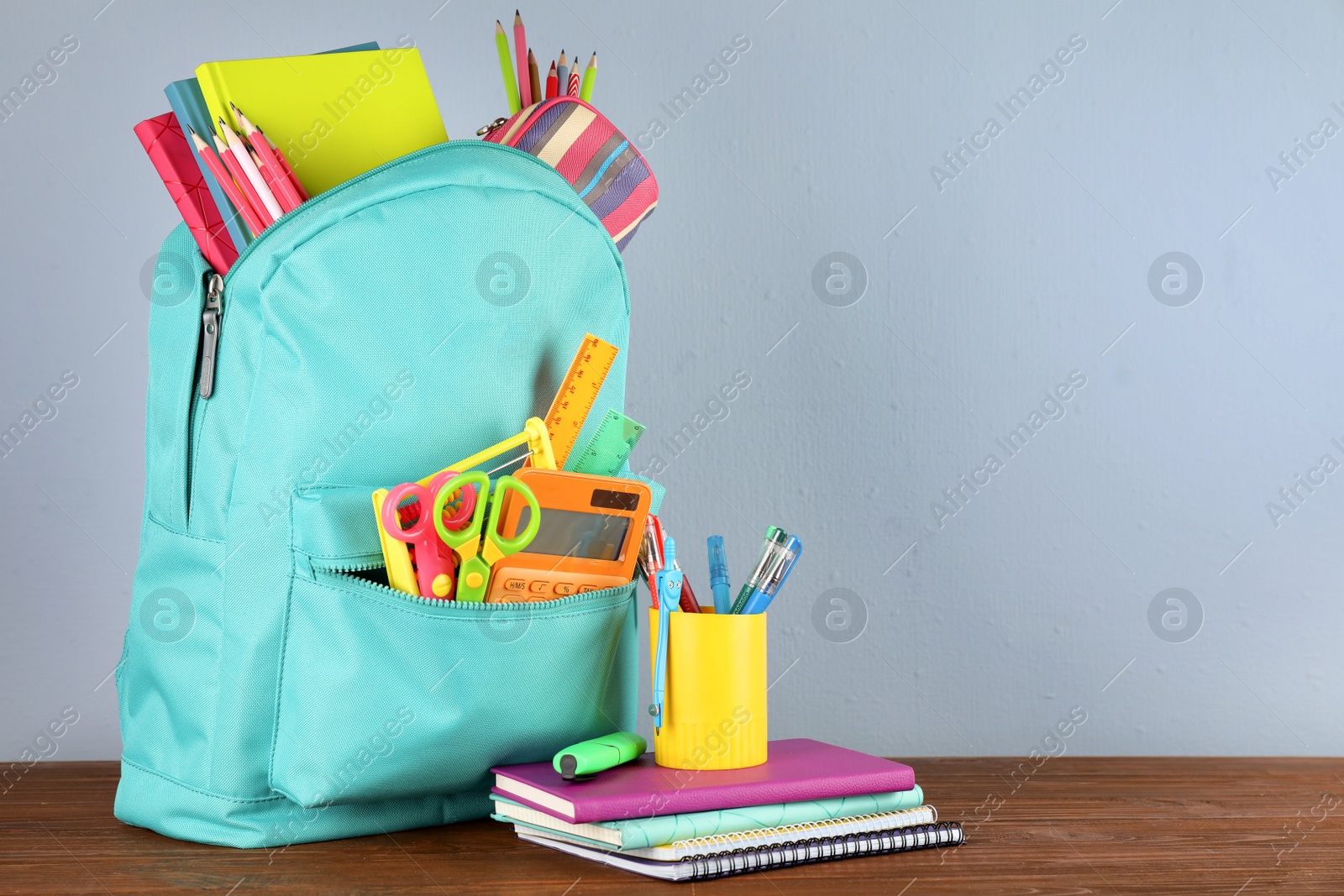 Photo of Bright backpack with school stationery on brown wooden table against grey background, space for text
