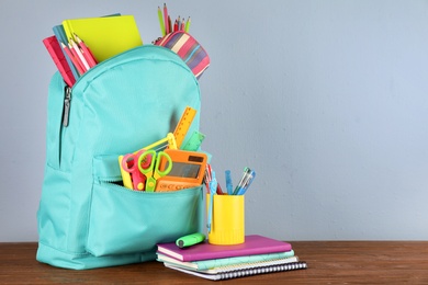 Bright backpack with school stationery on brown wooden table against grey background, space for text