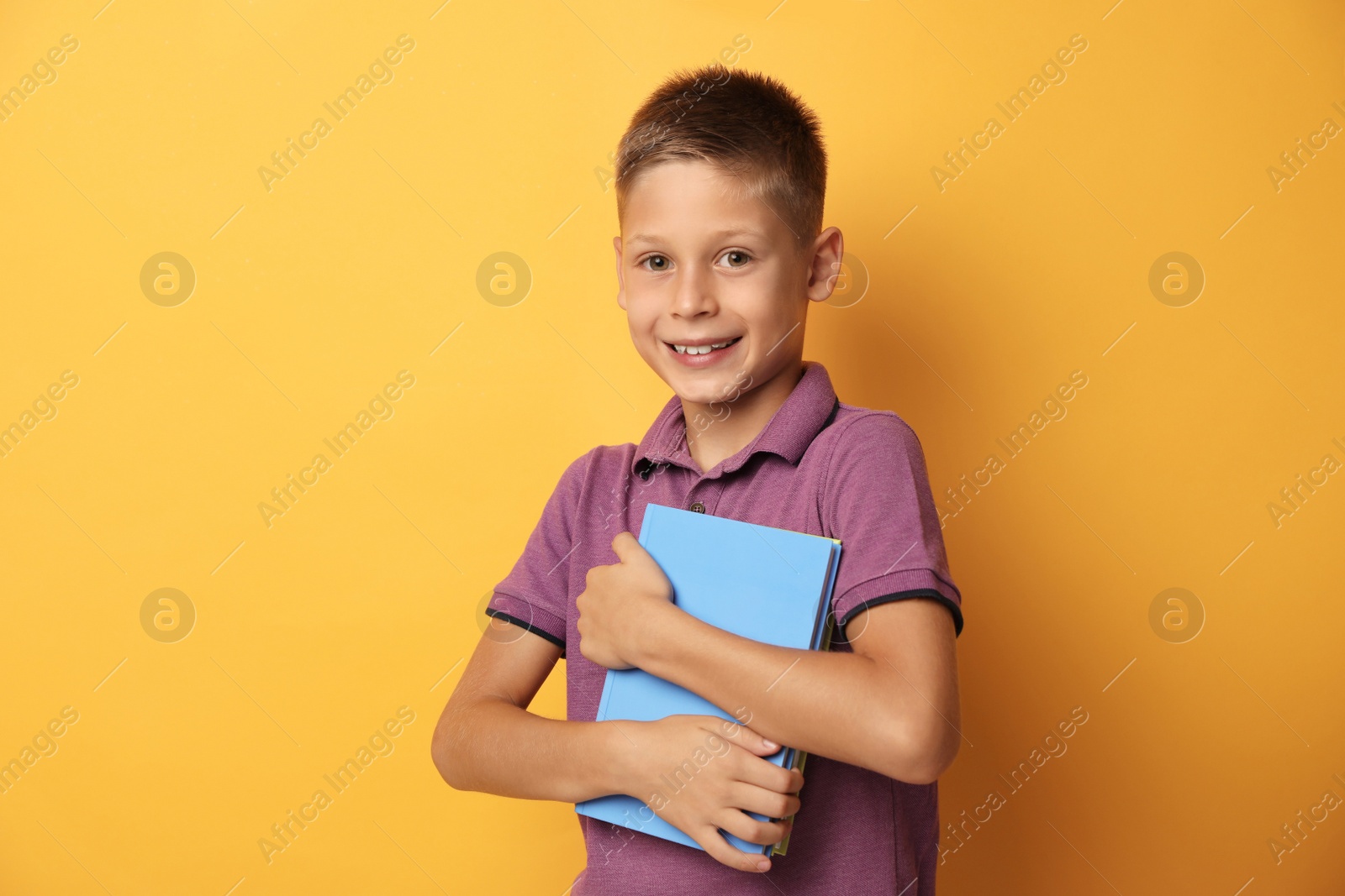 Photo of Portrait of cute little boy with books on yellow background. Reading concept