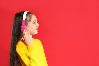 Cute girl enjoying music in headphones on color background. Space for text