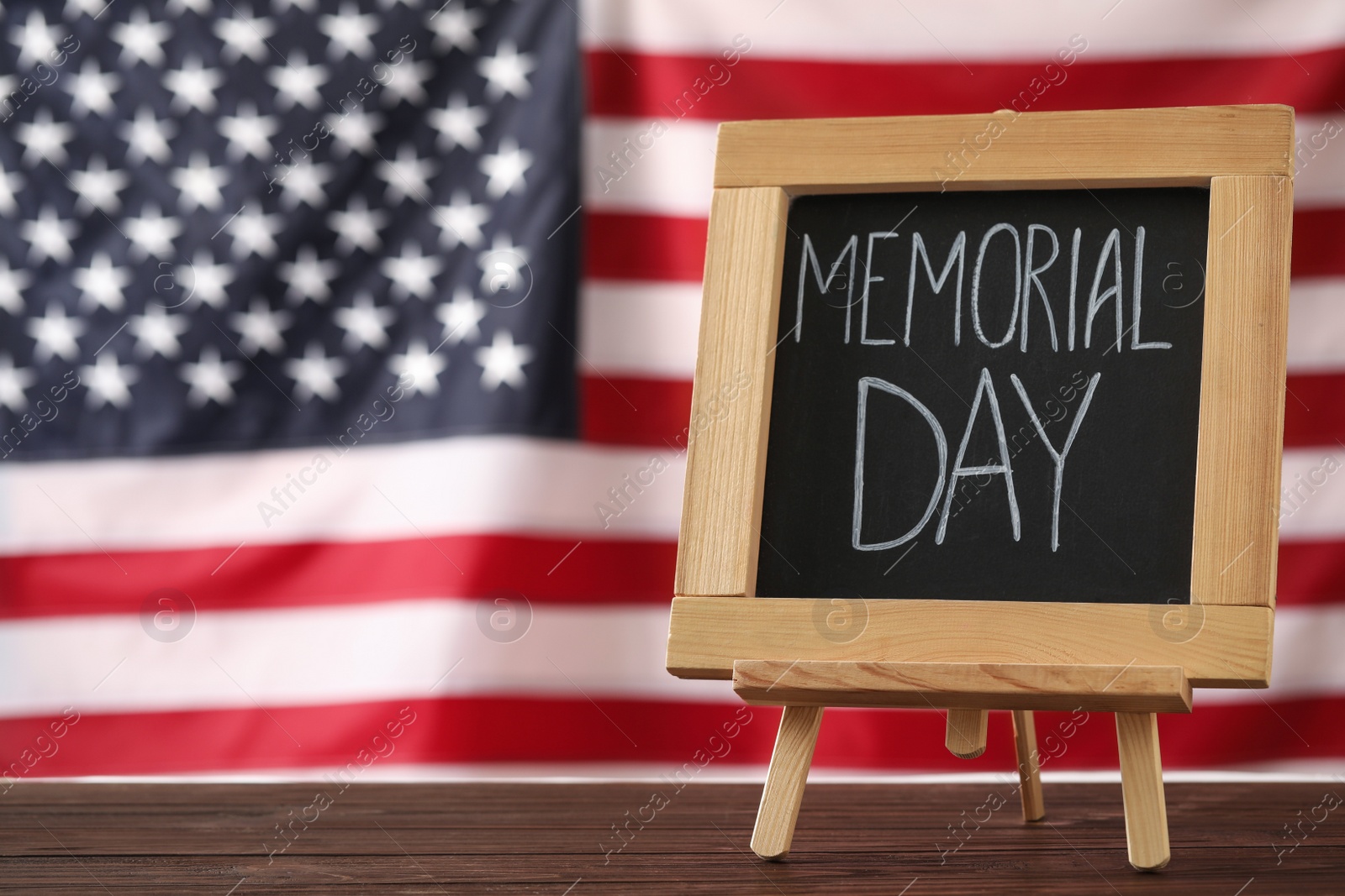 Photo of Blackboard with phrase Memorial Day on wooden table against American flag, space for text