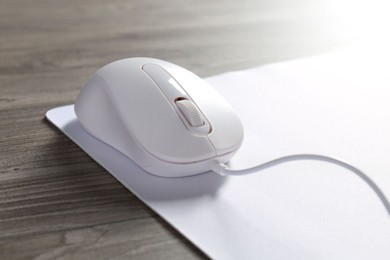 Photo of Wired mouse and mousepad on wooden table, closeup