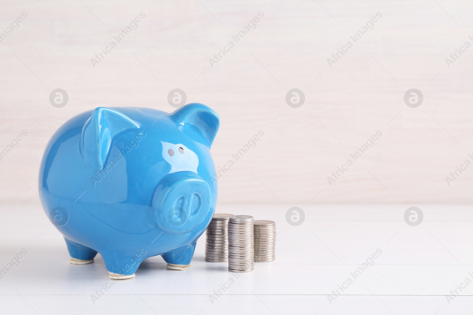 Photo of Financial savings. Piggy bank and stacked coins on white wooden table, space for text