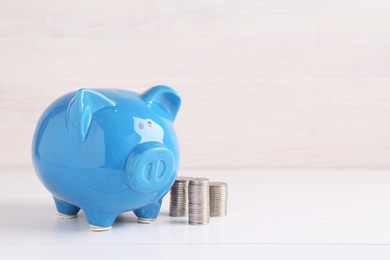 Photo of Financial savings. Piggy bank and stacked coins on white wooden table, space for text