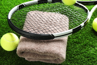 Photo of Tennis racket, towel and balls on green grass, closeup. Sports equipment