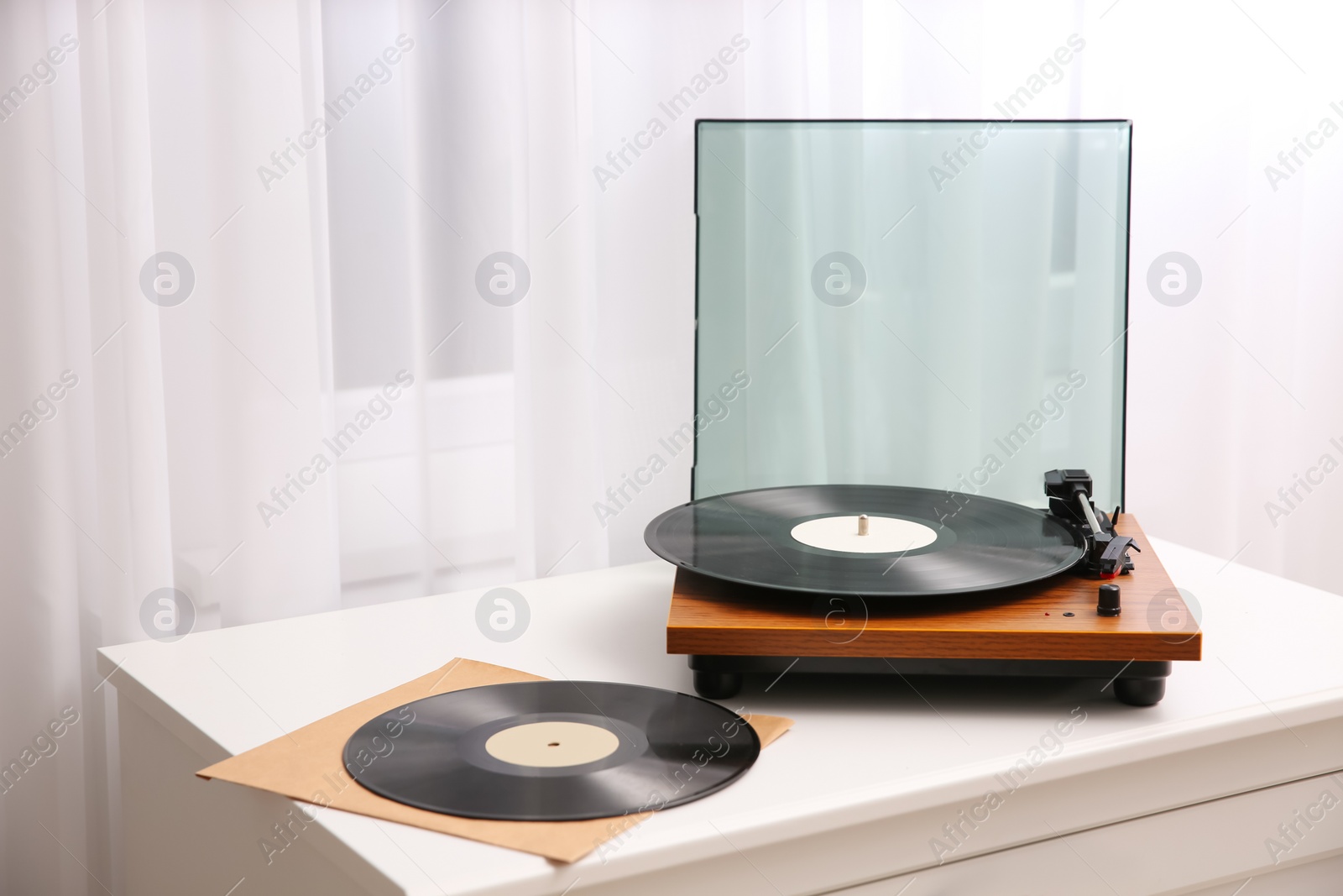 Photo of Stylish turntable and vinyl records on white chest of drawers indoors