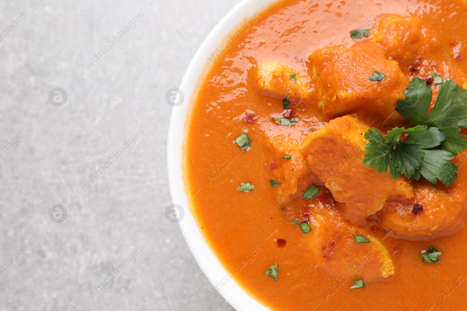 Photo of Bowl of delicious chicken curry on light grey table, closeup. Space for text