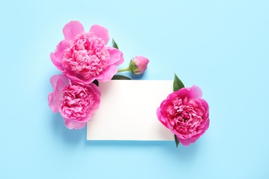 Fresh peonies and empty card on color background, flat lay with space for text