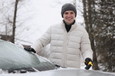 Photo of Man cleaning snow from car hood outdoors
