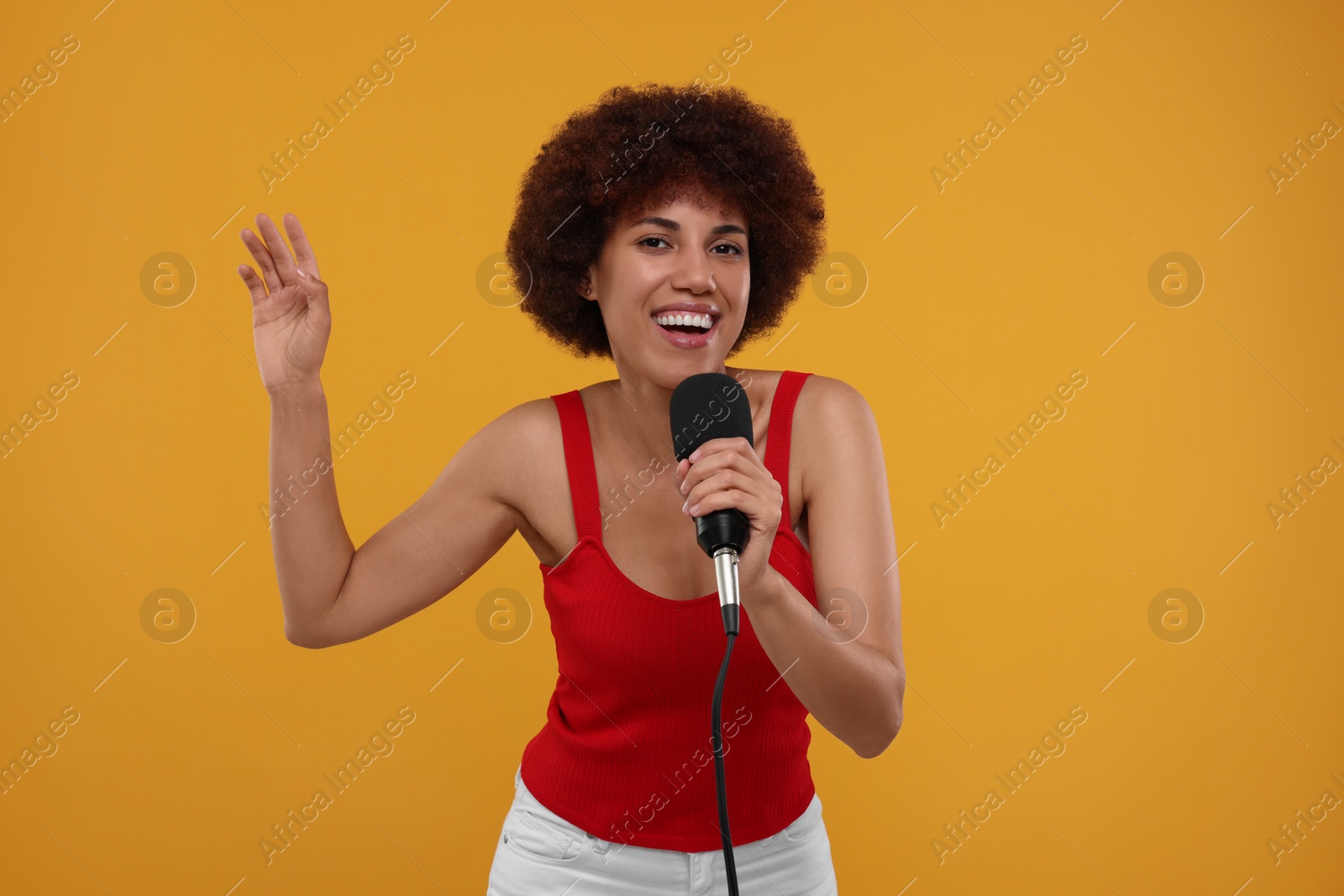 Photo of Curly young woman with microphone singing on yellow background